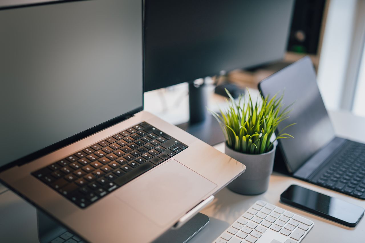 A sleek office workspace featuring a laptop, smartphone, keyboard, and potted plant for productivity.
